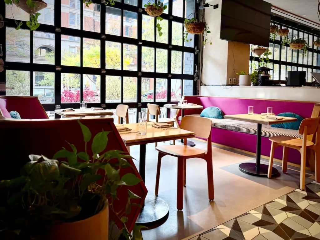 Michele's interior casual seating, Washington DC. The floor to ceiling windows are to the left with comfy pink sofas and chairs as well as wooden table and chair set-ups, creating an intimate and cosy space.