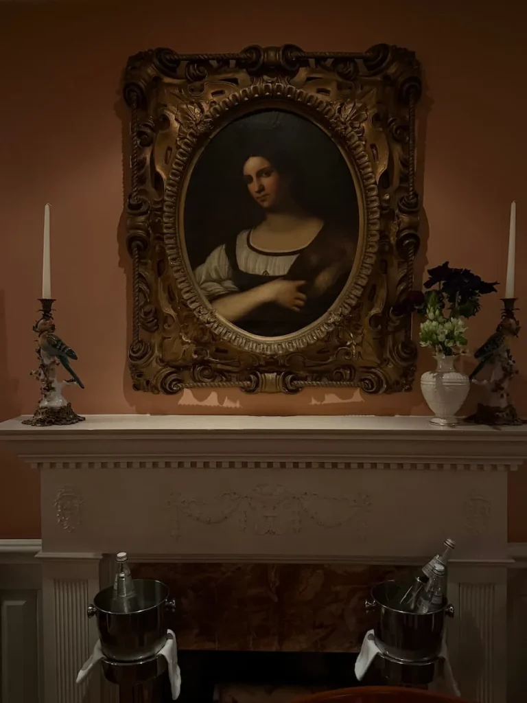 Painting over the marble fireplace at Elizabeths, Washington DC. The walls are a pale cream/pale oink colour above a marble fireplace with candle sticks and a delicate vase of flowers.