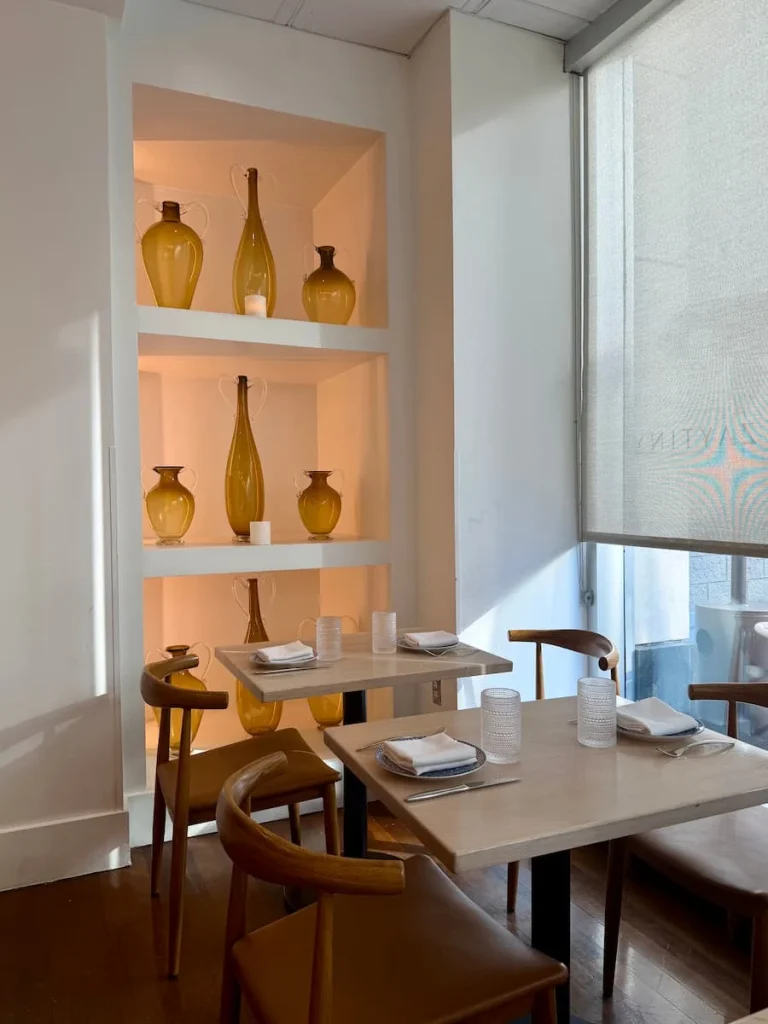 Seating and decor aat Zaytinya, Washington DC. The tables are a light wood with matching chairs. There is a shelf in the alcove with vases and down lighting