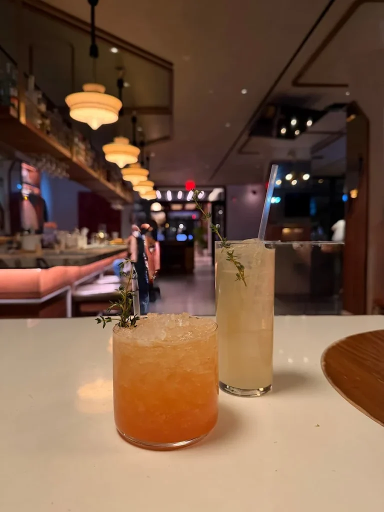 Spirit free cocktails at Michele's Washington DC. One is in a high ball glass and the other is orange in colour and in a smaller glass. the bar is in the background