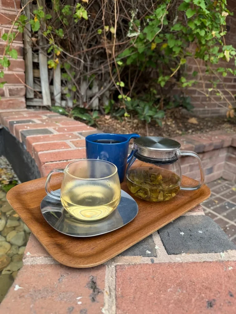 Jasmine yea in a glass cup and tea pot and a Coffee in a blue mug on a brown tray on a bricl wall in the courtyard at Flor in Washington DC
