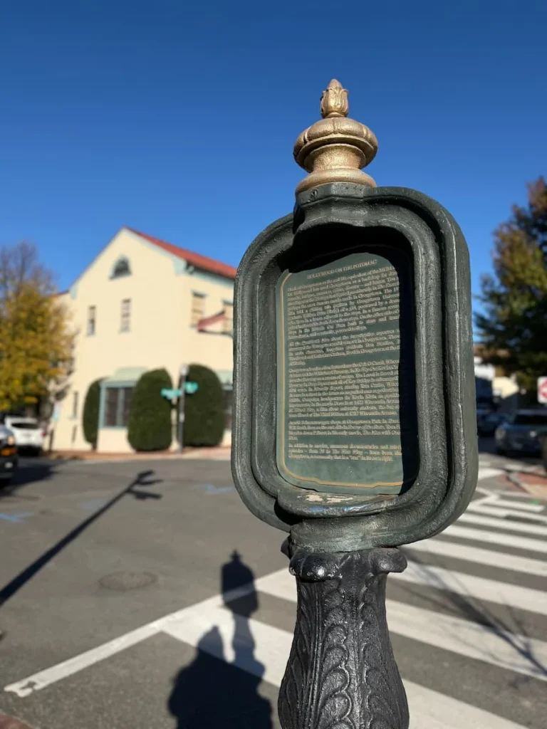 Exorcist Steps historic Plaque outside the restaurant in Georgetown, Washington DC with gold writing on a black background and a red frame. The street can be seen in the background