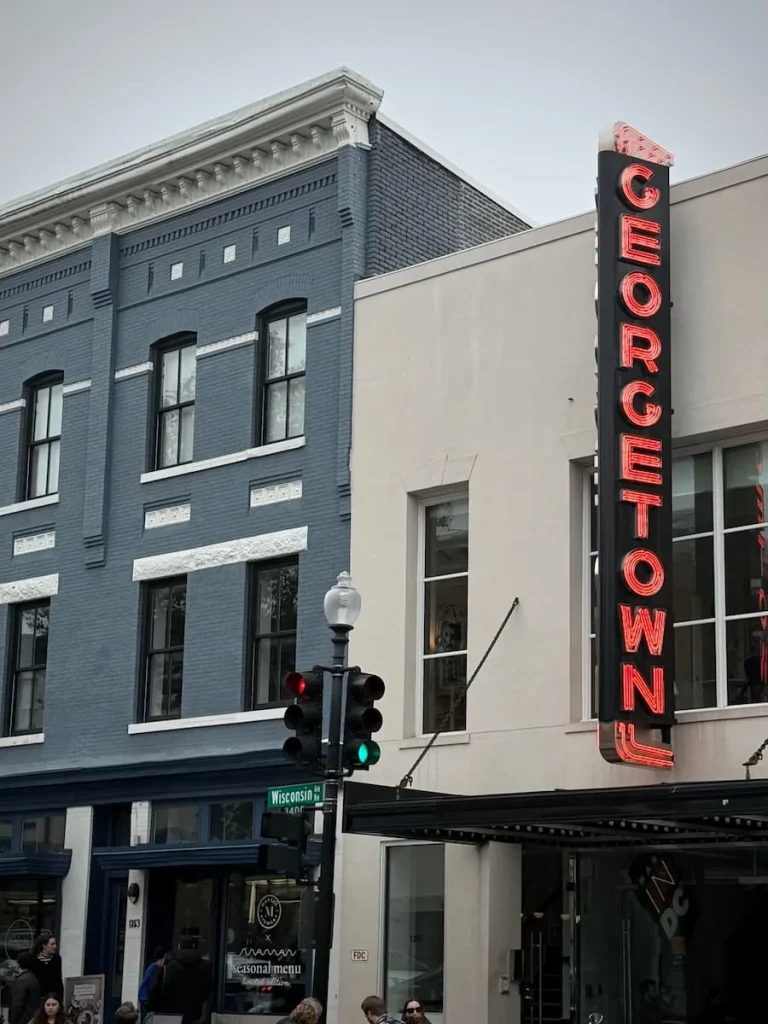 The Georgetown Neon Sign at Compass Coffee in Georgetown Washington DC. There are traffic lights just under it with people sitting outside enjoying their drinks