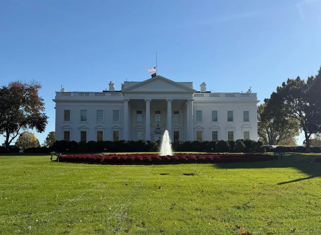 Exterior of teh The White House Washington DC with a fountain right infront and floral borders with trees to either side