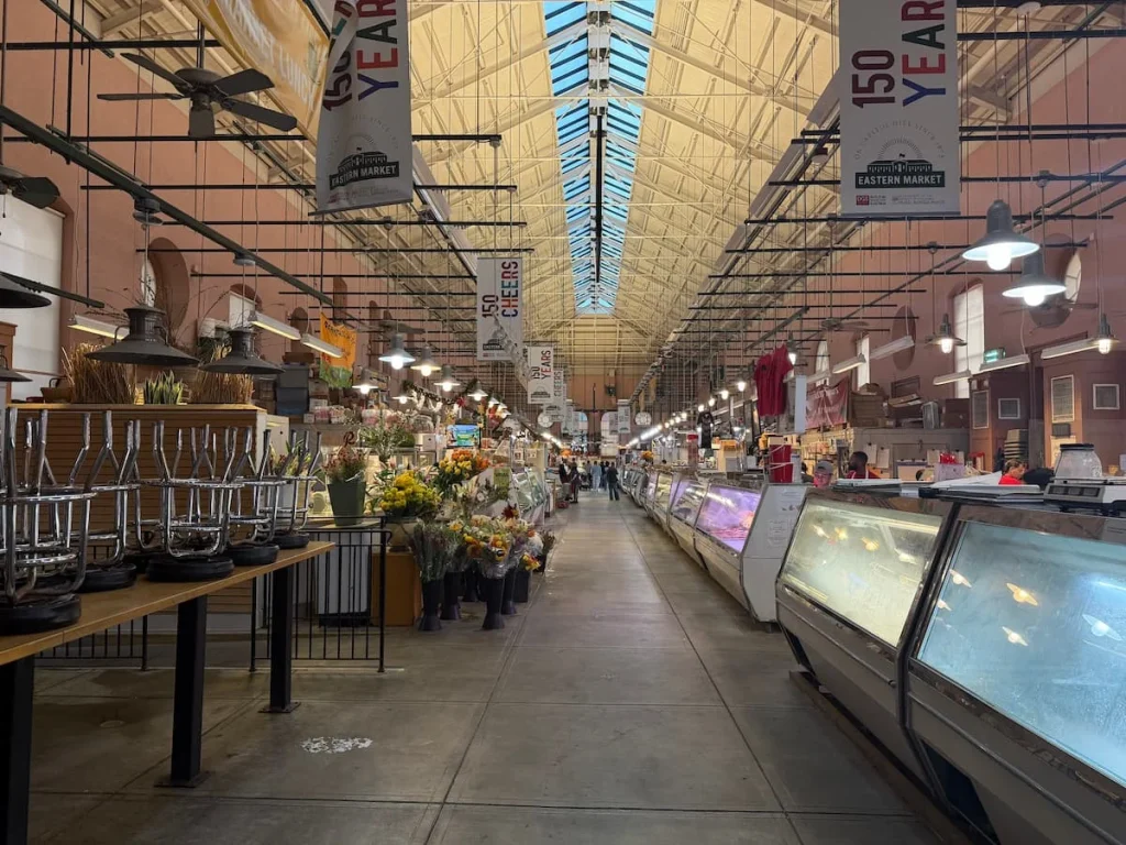 The aisle of the indoor Eastern Market with food and flowers at either side, Washington DC
