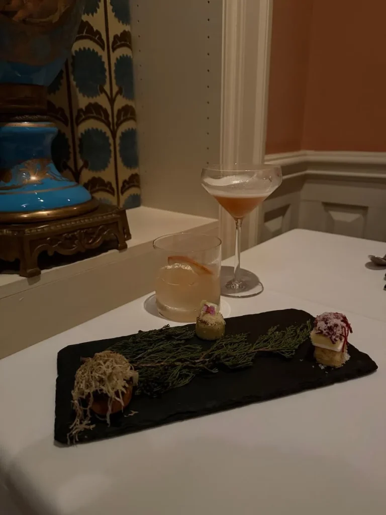 Trio of Amuse Bouche with two glasses of sparkling wine at Elizabeths, Washington DC on a white tablecloth next to an alcove with a blue and bronze vase