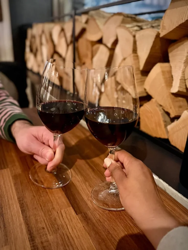 Two glasses of Punzi red wine doing a cheers at Via Sophia, Washington DC. There are 2 wooden cut logs in the background