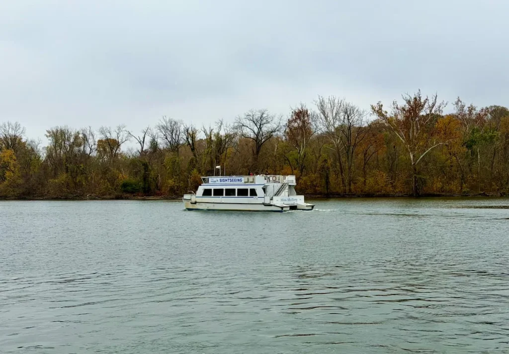 Water Taxi at The Waterfront in Georgetown Washington DC. The water taxi is white with two levels and has teh autumnal brown adn orange trees in the background