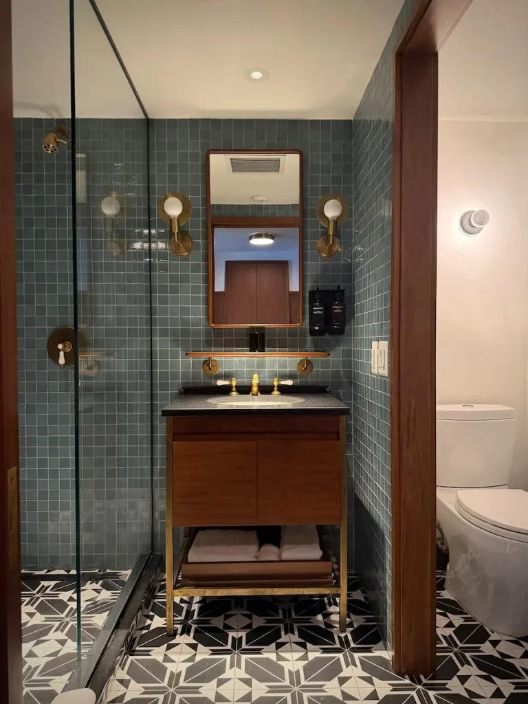 Bathroom sink and vanity unit at Eaton DC, Washington DC, The teal and dark grey mosaic tiles are on teh walls contrasting against the dark wood furniture of the vanity unit