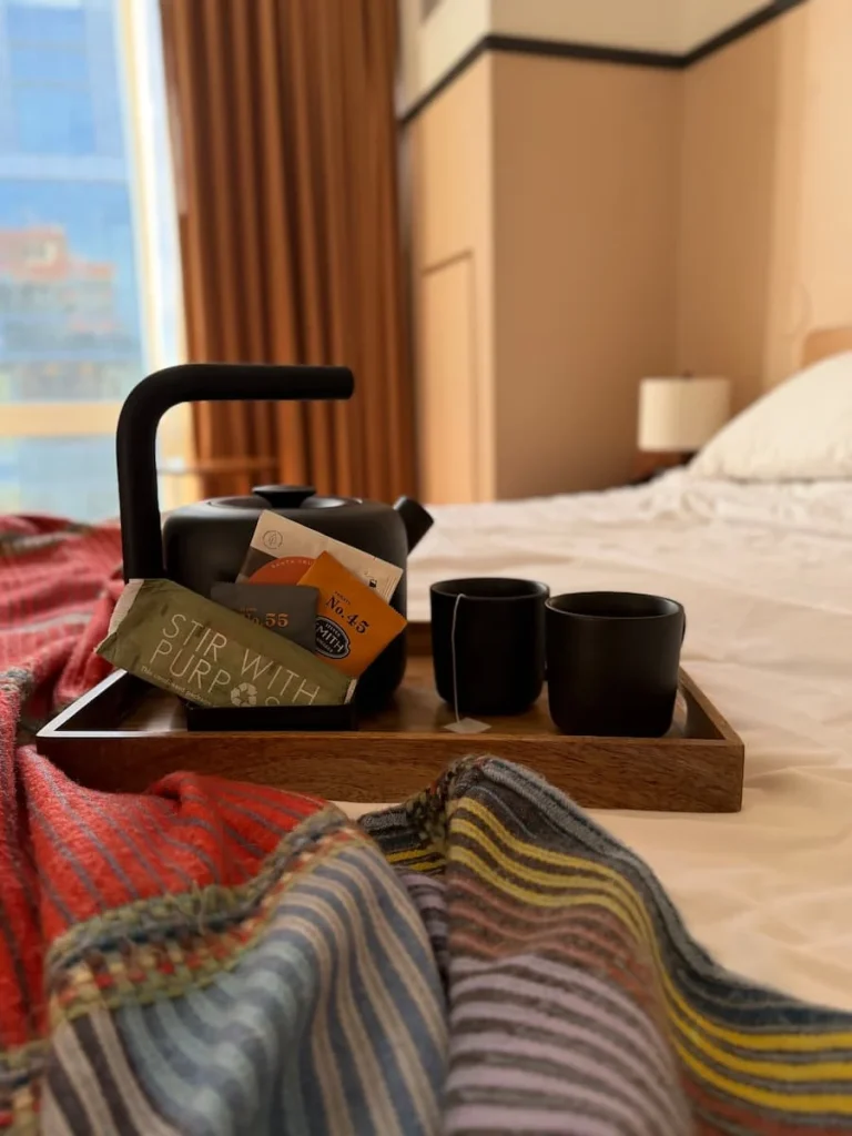 Kettle and tea tray on bed in room at at Eaton DC, Washington DC. There is a colourful blanket underneath