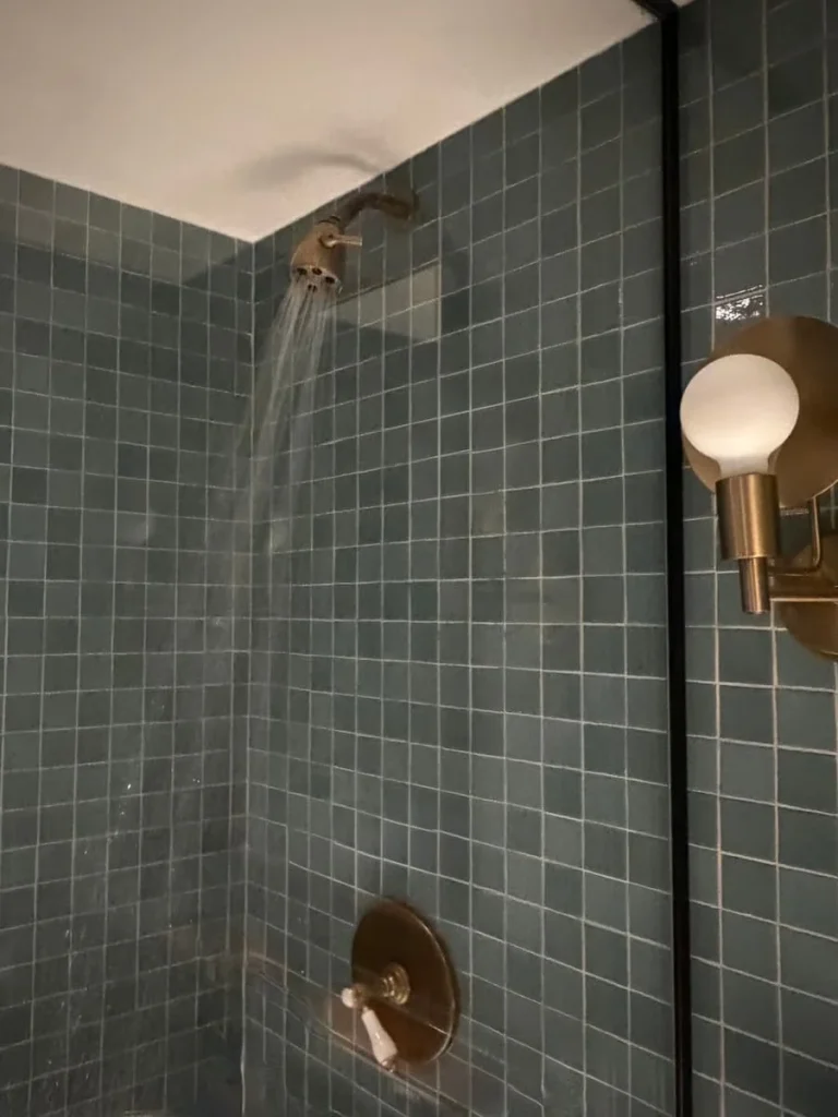 Shower cubicle with water running at Eaton DC, Washington DC. The cubicle has teal coloured mosaic tiles and a gold shower head