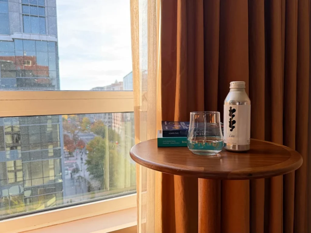 Water bottle and glass with water at Eaton DC, Washington DC. The pink curtain and views of the street can be seen in the window in the background