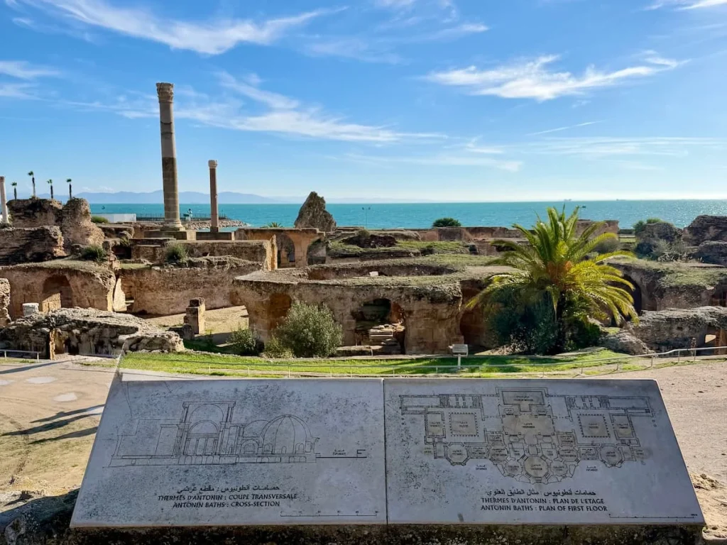 One day in Sidi Bou Said, a Carthage day trip. Antoninian Baths, Carthage, Tunisia landscape. The Mediterranean sea is in the background with the ruins in front and a detailed plan board explaining the site.