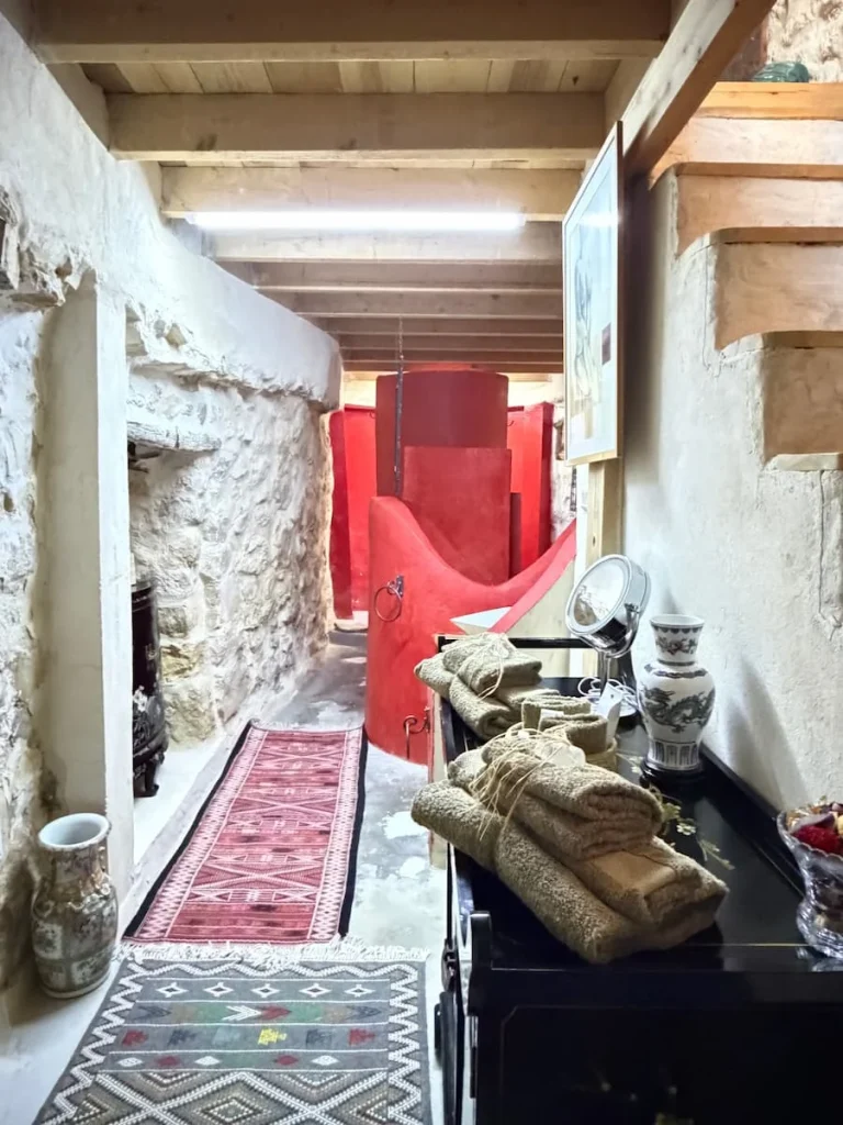 Bathroom at Toumadir Suite at L'Auberge de Tamezret. The background paint is red and there are antique side boards with towels and bath products on