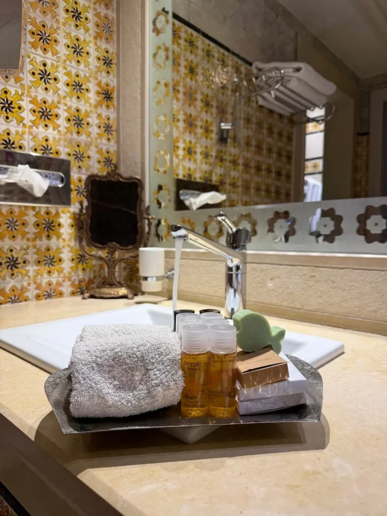 Bathroom toiletries at Dar Alouini, Kairouan, Tunisia. There are small bottle sof bath products, soaps, flannels and the mosaic tiles in the background.