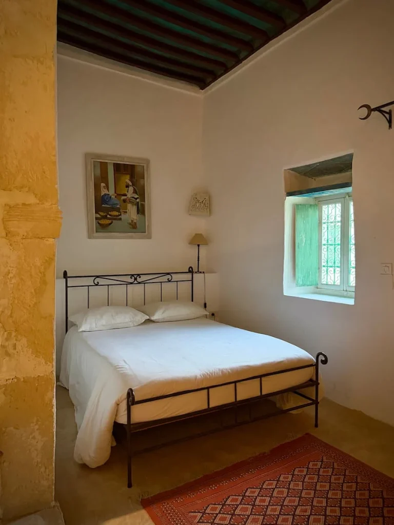 Wrought iron bed at Dar Dhiafa with white linen and painting above, Djerba