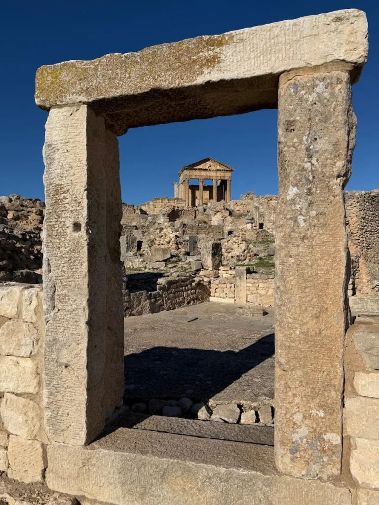 The Capitol inside a stone frame at Dougga, Tunisia. Bright blue skies are nehind the ruins