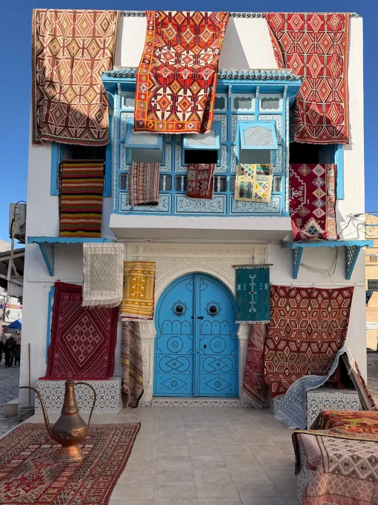 colourful Carpet shops in Kairouan Medina, Tunisia. Rugs and carpets hang outside the double blue studded door on the ground floor and first floor.