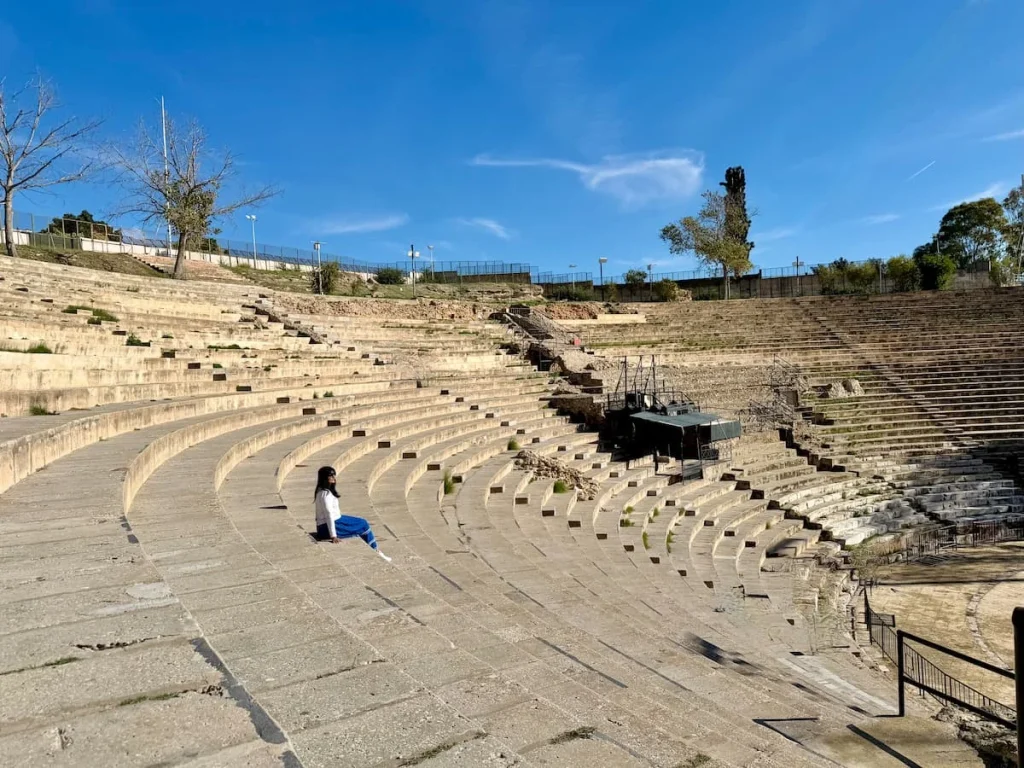 Bejal sitting on the steps on the Carthage Amphitheatre wearing a cream top and blue skirt