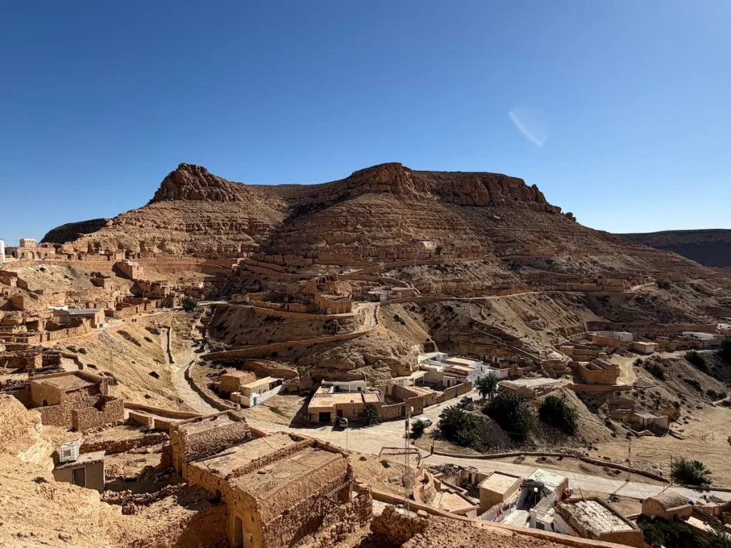 A panoramic photo of Chenini, Berber Town located in southern Tunisia, with houses cut into the rock. The bright blue sky shines above the town