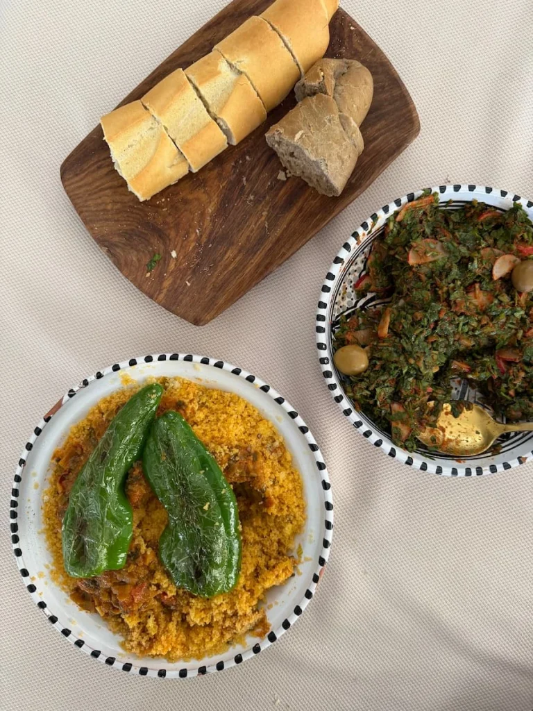 Top Lay of Lunch at Dar Yomma. The white table cloth has locally made pottery dishes, with some bread, couscous with vegetrables and green chilli peppers and a traditional salad from the area of Tozeur.