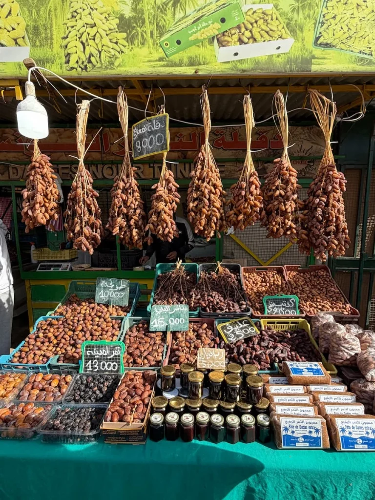 A Date stall in Tozeur Market, Tunisia. The Dates are laid out on the covered table as well as hung in. bunches from the roof of the stall.