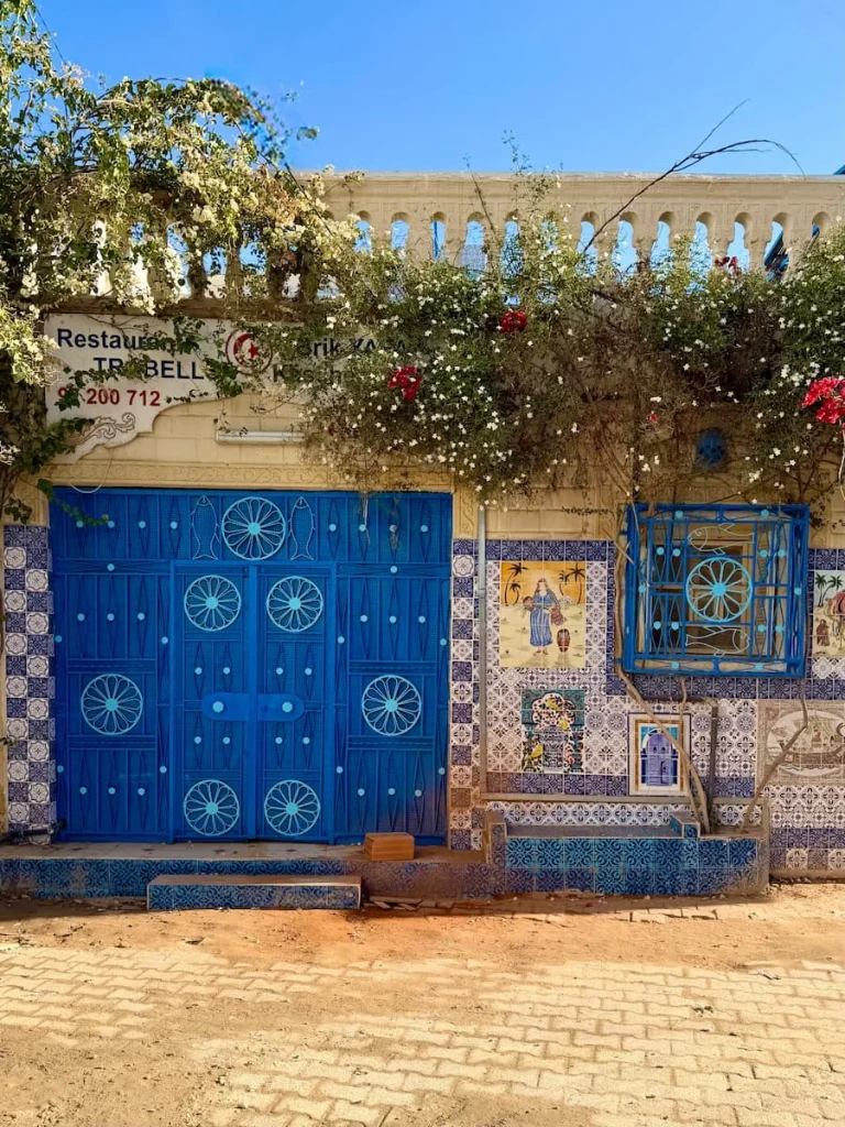 Djerba streets and restaurants. There is a big blue door with a blue framed window and bougainvillaea growing over the facade of the restaurant