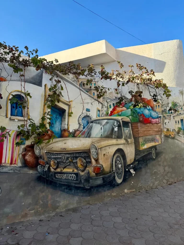 Djerbahood street art, Djerba Tunisia. The mural is of a colourful truck willed with thing sin the back and is painted against the blue and whitewashed houses.