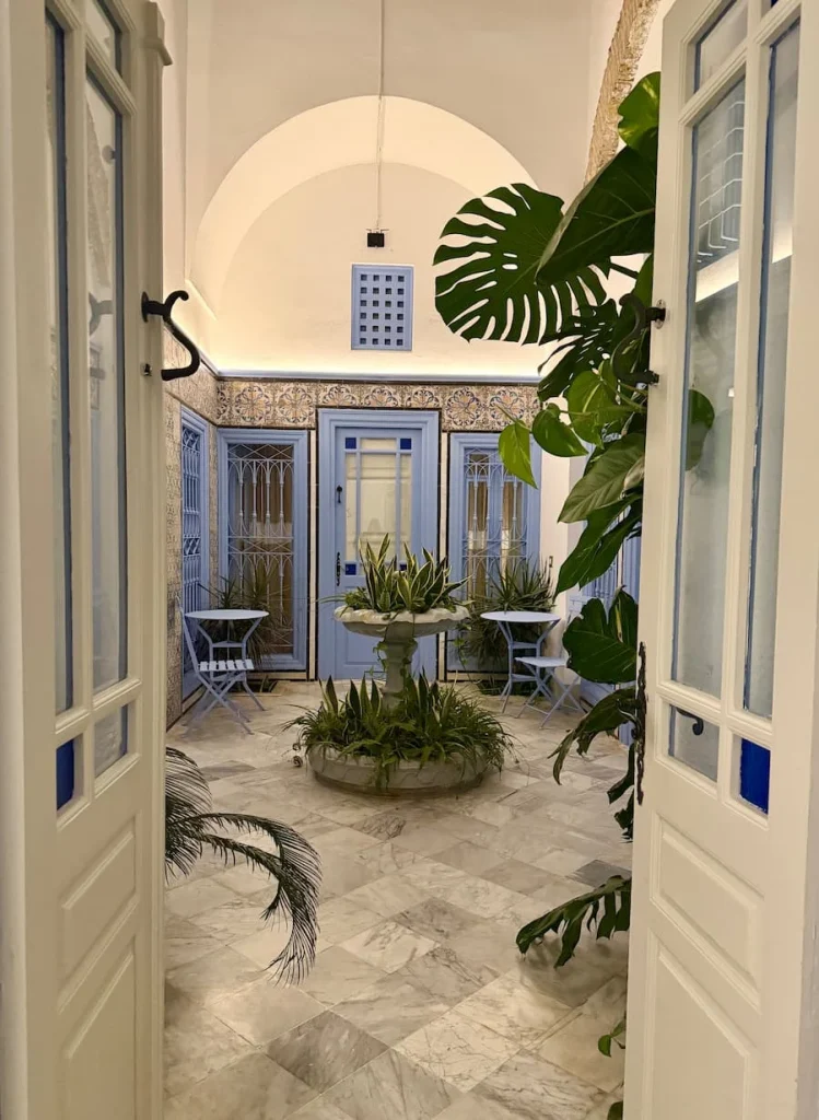 Double white doors into internal courtyard at Dar Said, Tunisia. The courtyard is covered in colourful mosaics and foliage