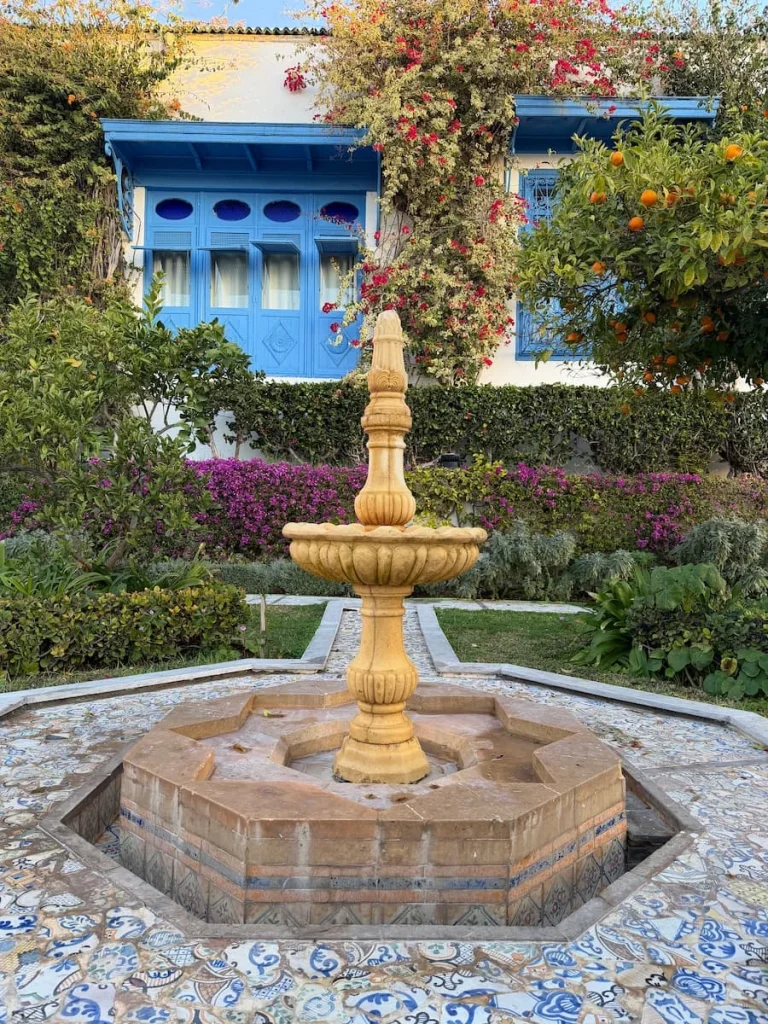 Light brown fountain in Dar Said Garden, Sidi Bou Said. There is bougainvillaea and bushes and plants in the background, Tunisia