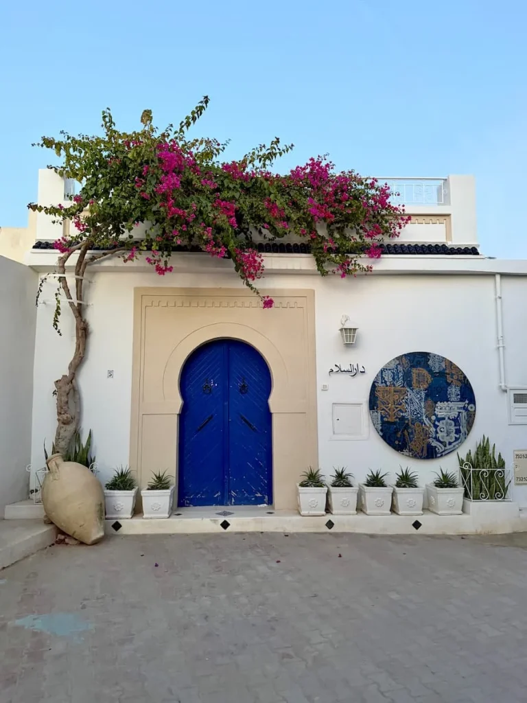 Hara Sghira Er Riadh, Djerba, Tunisia with a blue door, street art circular design and draped bougainvillaea on the roof.