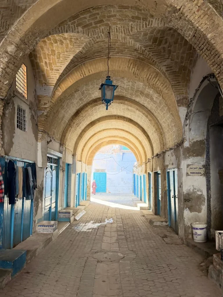 Kairouan Medina archways with a man walking through in the distance dressed in light brown traditional outfit