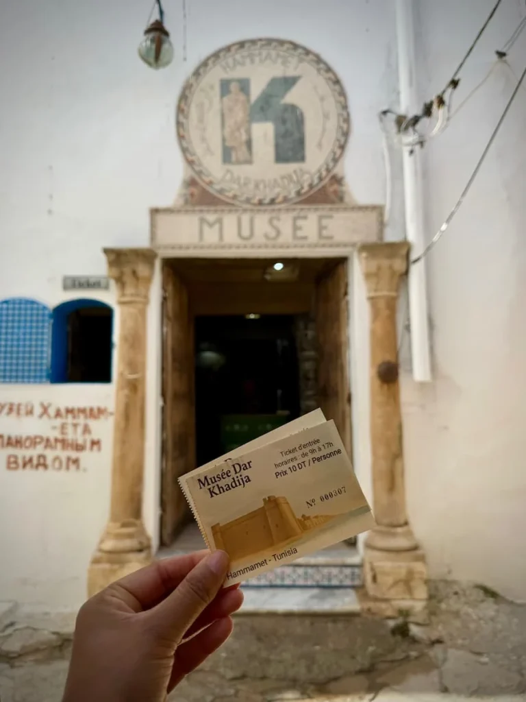 Bejal holding Tickets to the Khadija museum in the Hammamet Medina, with the museum door in the background