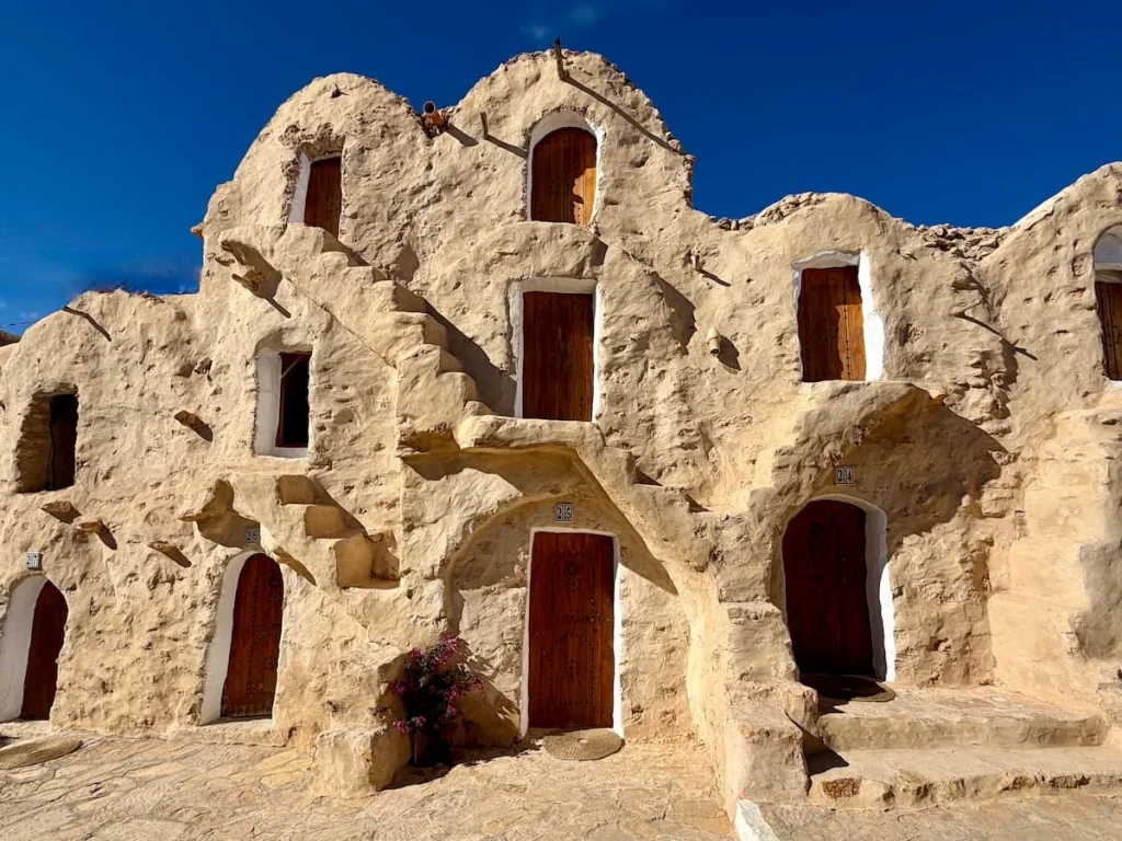 Ksar Hedada showing how well preserved the site is. Triple story houses with stairs connecting each floor on the exterior. The building is a pale sand colour against the bright blue sky