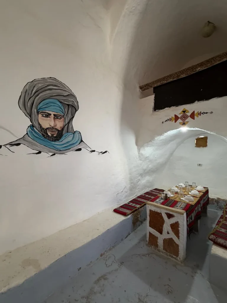 Ksar Hedada restaurant, Tunisia. The white washed walls have an image of an Arab main painted on the wall. There is a table set for diners to the right