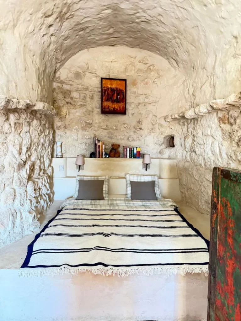 L'Auberge de Tamezret bedroom, Tunisia. The bed is built into the white cave-like structure of teh house in Matmata. There are colourful linens and blankets on the bed