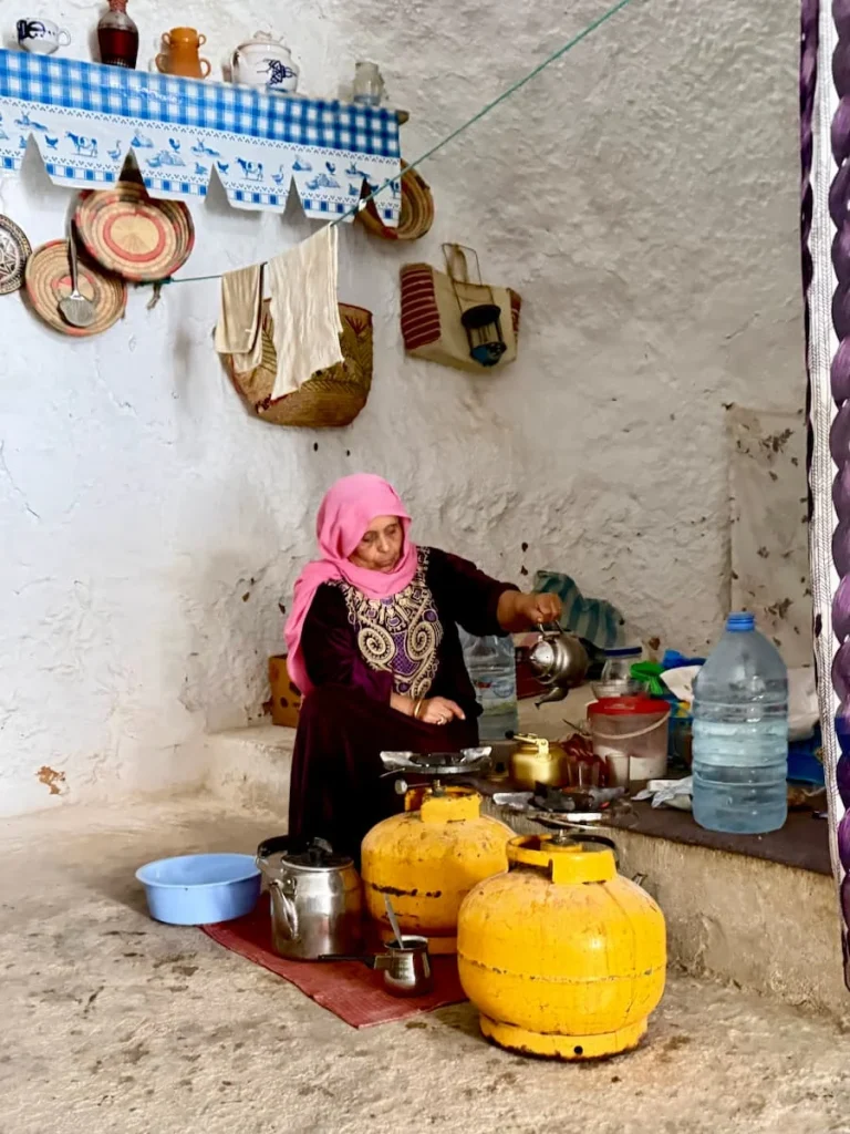 Lady wearing a pink headscarf with traditional dress making tea in Troglodyte House in Matmata, Tunissa