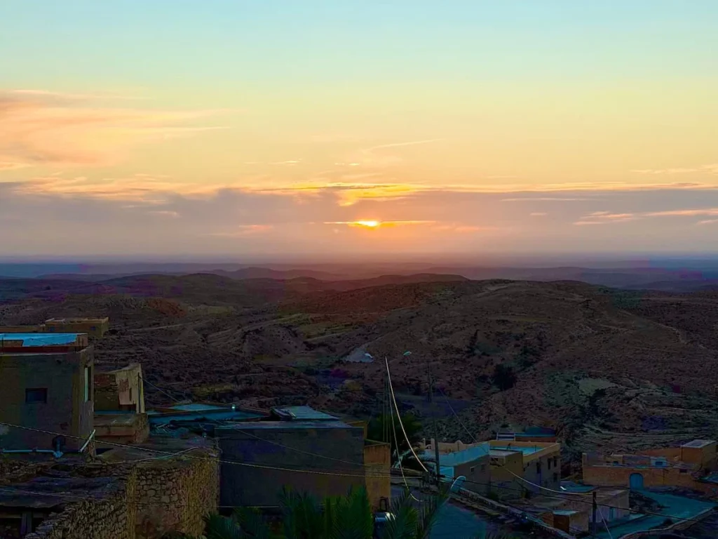 Matmata mountains in the background with a sunset. There are other houses in the surrounding area