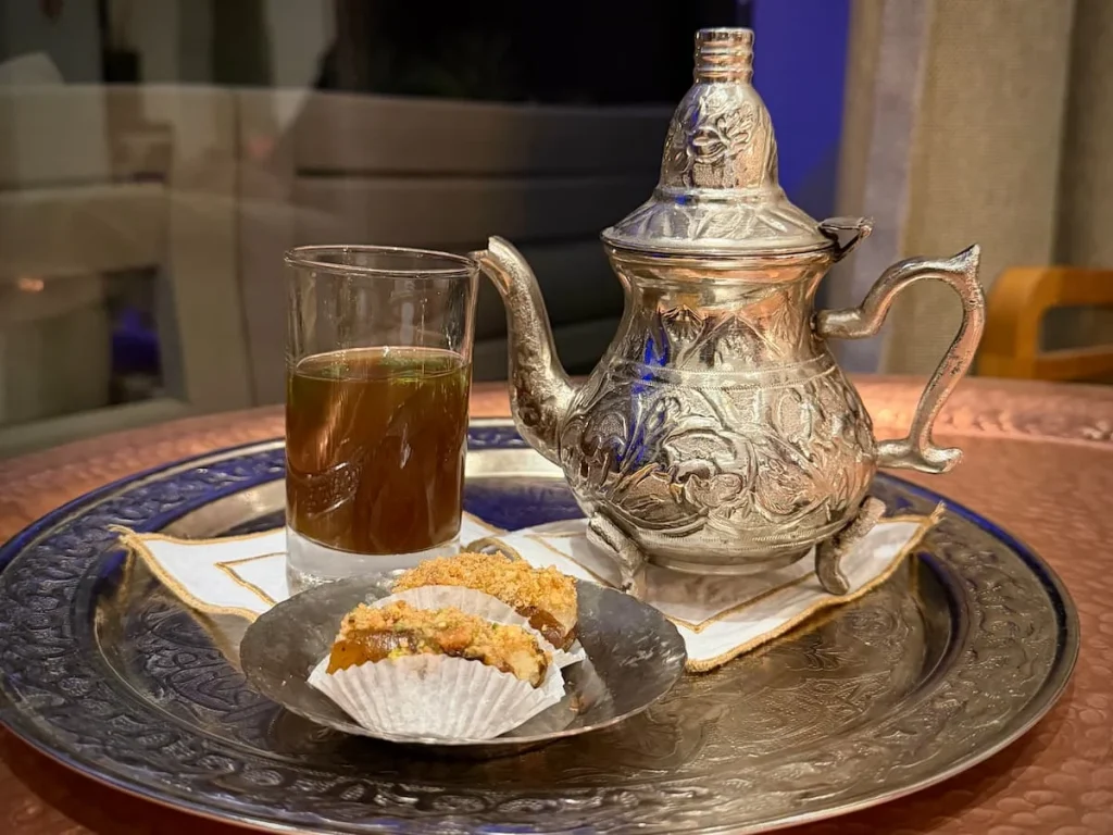 Mint tea in a decorated silver tea pot placed on a tray with a small cup filled with tea and sweet date snacks at The Mora Tozeur, Tunisia