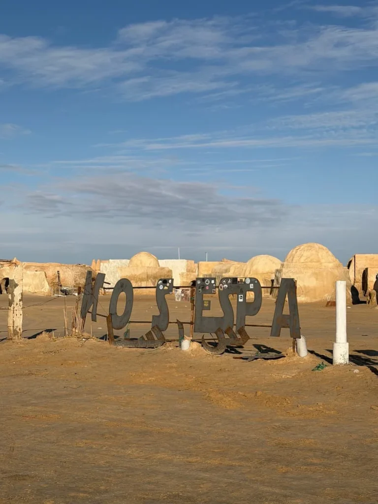 The Mos Espa Sign in Tunisia. The sign is made from metal letters with the site behind it with desert hues and bright blue skies