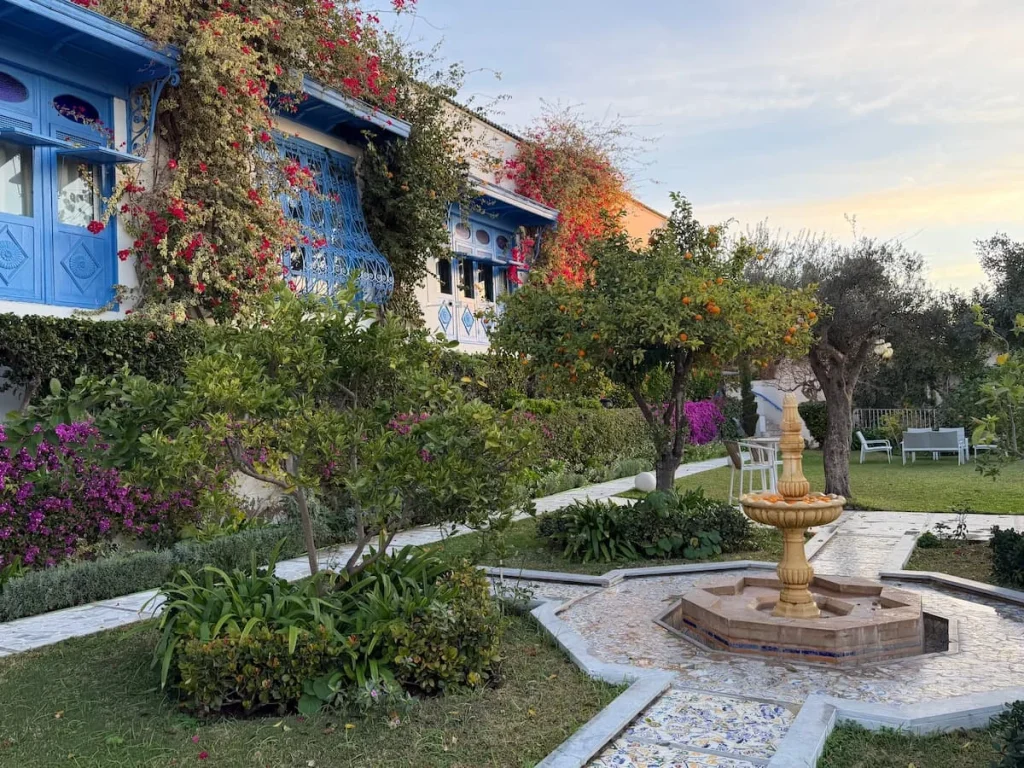 Outdoor garden at Dar Said, Sidi Bou Said. There is a fountain to the right and the hotel wall is covered in green foliage and bougainvillaea with Mashrabiya windows overlooking the garden