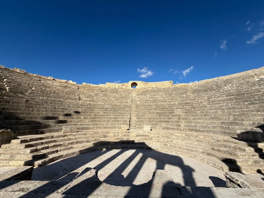 Panoramic of Dougga Amphitheatre, Tunisia with its tiered stone seating against a brighy blue sky