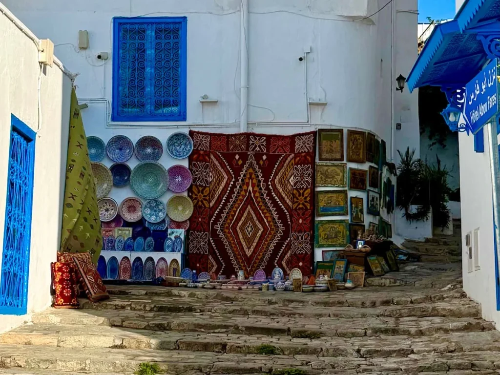 Pottery and Carpets shop in alleyway in Sidi Bou Said, Tunisia. The pates are different bright colours as are the rugs draped on a white washed house.