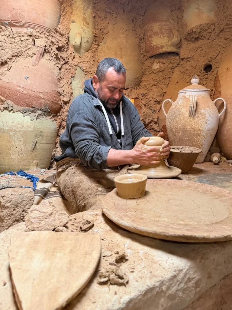 A potter at Ben Mimoune Pottery making an ash tray using the potter's wheel. Potter is wearing a grey hoodie and is holding the partially finished ash tray