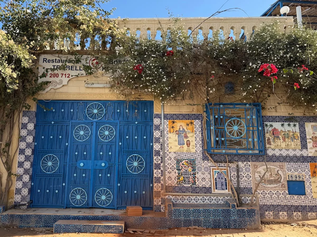 Pretty blue door restaurant fascia in Djerba. The exterior has lots of green foliage and bougainvillaea growing at the top