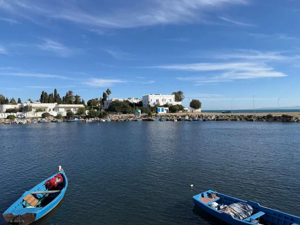 Punic Ports of Carthage with multicolour fishing boats on teh deep blue hued sea and remnants of old buildings