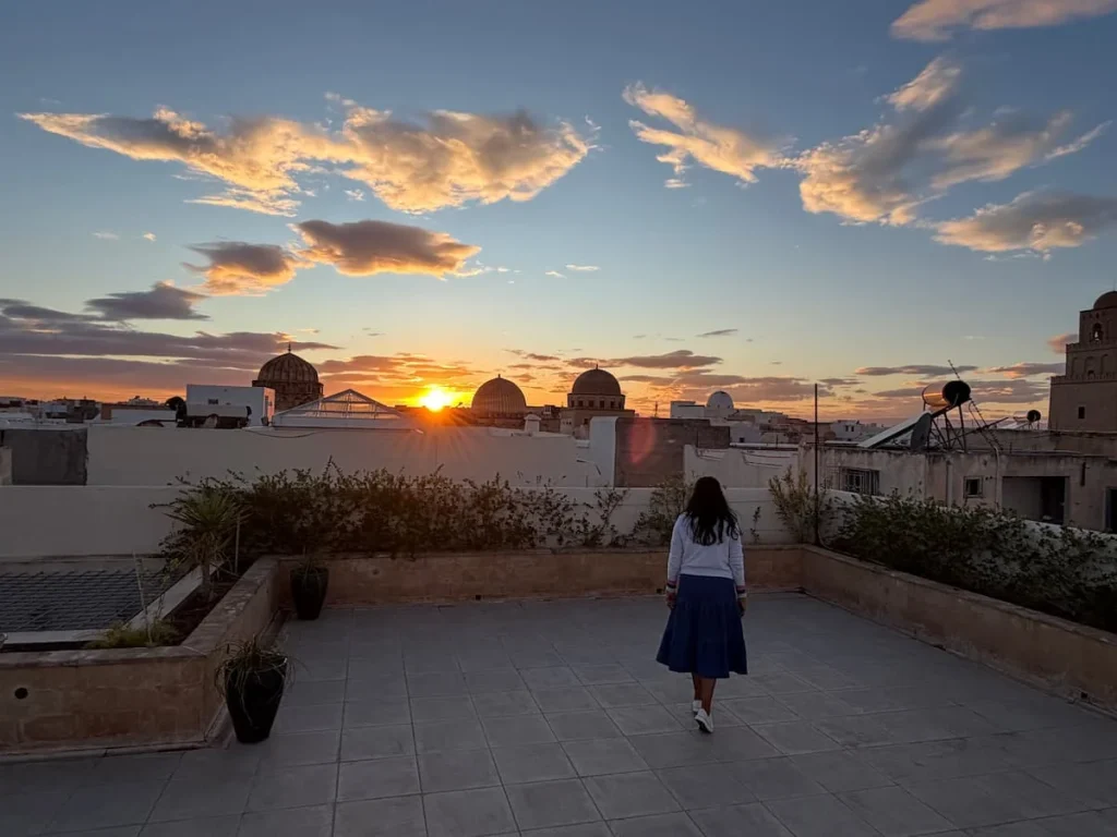 Bejal wearing a white jumper and blue skirt walking towards the sunset on Dar Alouini rooftop, Tunisia