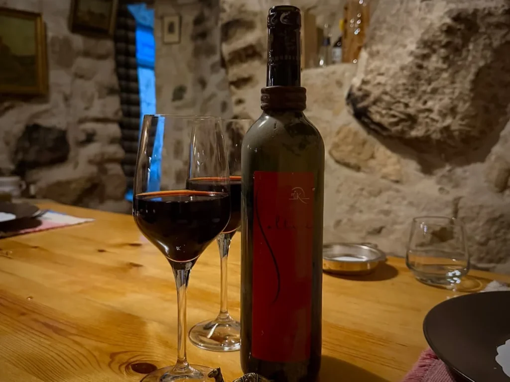 A bottle of Tunisian red wine and 2 glasses os red wine on a wooden table at L'Auberge de Tamezret, Tunisia
