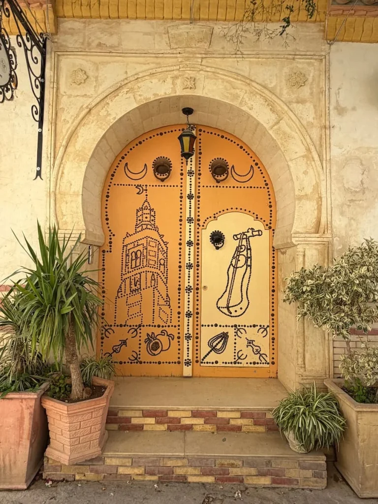 Typical yellow Testour Door with studded minuret and local instrument. There are potted plants outside the door