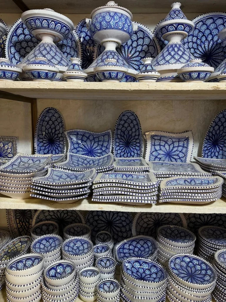 Things to do in Djerba: Ben Mimoune Guellala Potteries in Djerba with white and blue pottery items on shelf including, trays, ashtrays and small bowls
